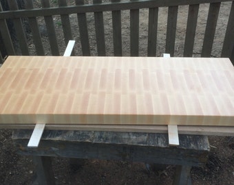 May include: A large, rectangular, wooden cutting board with a light brown color and a striped pattern. The board is resting on a wooden table.
