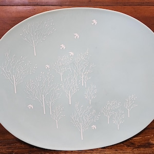 May include: A light blue oval ceramic serving platter with a white design of trees and birds.
