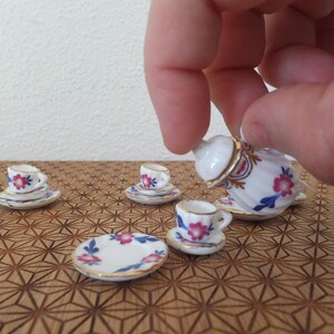 May include: A miniature tea set with a white teapot, cups, and saucers. The set features a floral pattern in pink, blue, and gold.