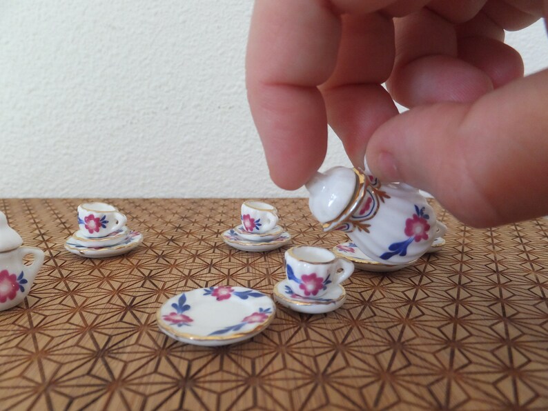May include: A miniature tea set with a white teapot, cups, and saucers. The set features a floral pattern in pink, blue, and gold.