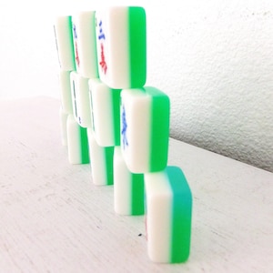 Puede incluir: Una pila de fichas de Mahjong blancas y verdes. Cada ficha tiene un centro blanco con bordes verdes. Algunas fichas tienen caracteres chinos rojos y azules. Las fichas est&aacute;n dispuestas sobre una superficie blanca.