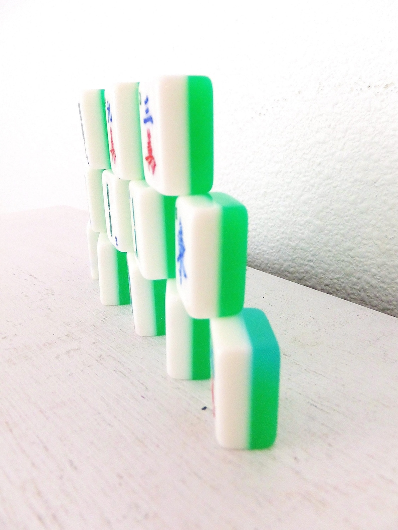 Puede incluir: Una pila de fichas de Mahjong blancas y verdes. Cada ficha tiene un centro blanco con bordes verdes. Algunas fichas tienen caracteres chinos rojos y azules. Las fichas est&aacute;n dispuestas sobre una superficie blanca.