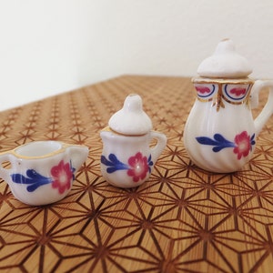 May include: A miniature tea set with a white teapot, creamer, and sugar bowl. Each piece features a blue and pink floral design.