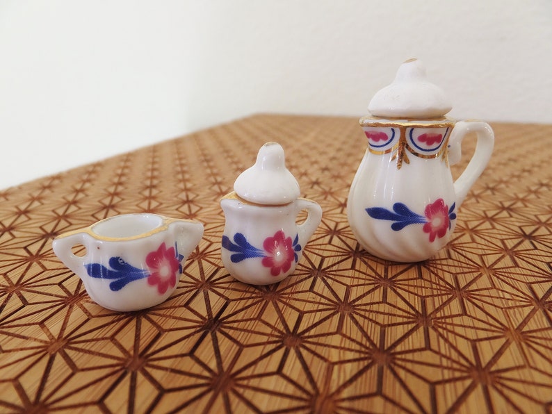 May include: A miniature tea set with a white teapot, creamer, and sugar bowl. Each piece features a blue and pink floral design.