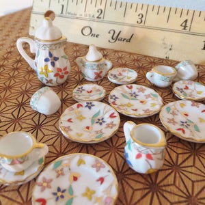 May include: A miniature porcelain tea set with a floral design. The set includes a teapot, creamer, sugar bowl, four teacups, and four saucers. The set is decorated with colourful flowers and gold trim.