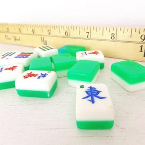 Puede incluir: Un conjunto de fichas de Mahjong blancas y verdes con s&iacute;mbolos rojos y azules. Una regla de madera con medidas en pulgadas est&aacute; en el fondo. Las fichas est&aacute;n dispuestas sobre una superficie blanca.