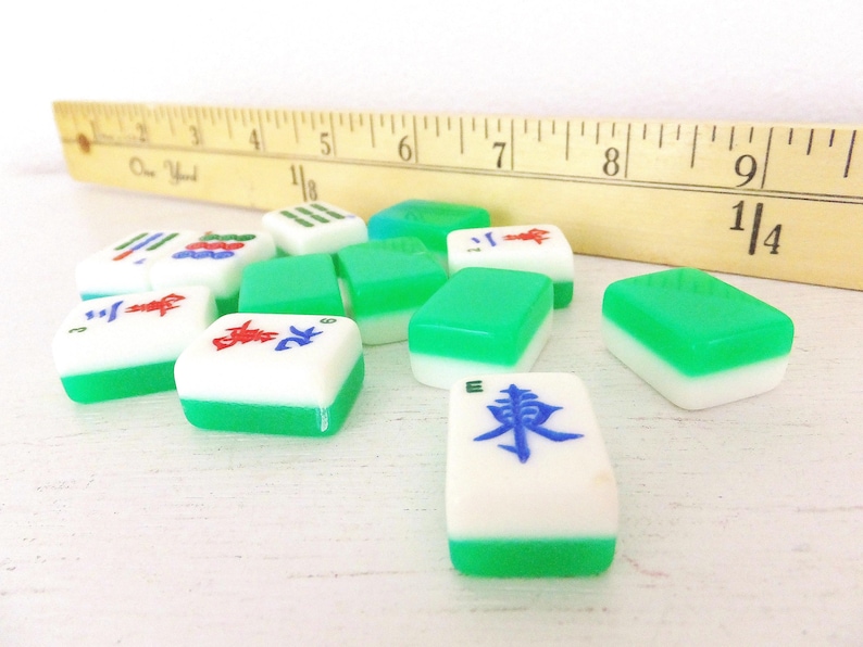 Puede incluir: Un conjunto de fichas de Mahjong blancas y verdes con s&iacute;mbolos rojos y azules. Una regla de madera con medidas en pulgadas est&aacute; en el fondo. Las fichas est&aacute;n dispuestas sobre una superficie blanca.