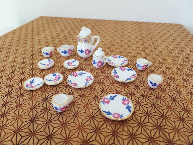 May include: A miniature tea set with a white background and pink and blue floral designs. The set includes a teapot, creamer, sugar bowl, cups, and saucers.