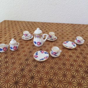 May include: A miniature tea set with a white teapot, creamer, sugar bowl, and four teacups and saucers. The set features a floral pattern with pink and blue flowers and gold accents.