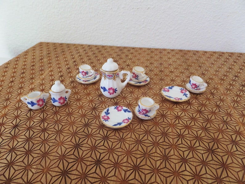 May include: A miniature tea set with a white teapot, creamer, sugar bowl, and four teacups and saucers. The set features a floral pattern with pink and blue flowers and gold accents.