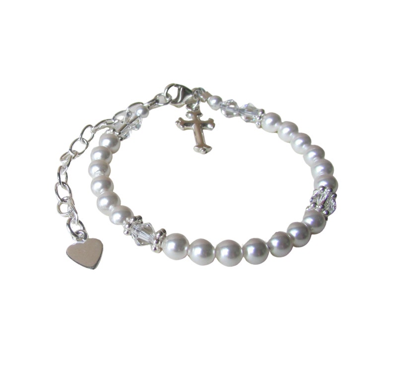 May include: A silver bracelet with white pearls, a small silver cross charm, and a silver heart charm.