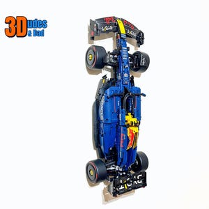 May include: A blue, black, and yellow Formula 1 race car model. The model has the text "BYBIT" and "ORACLE" on it. The image also includes the text "3Dudes & Dad".