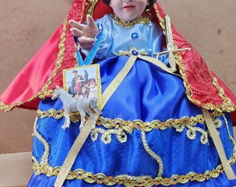 Puede incluir: Una figurita de un niño pequeño vestido como un caballero, con una túnica azul y dorada con una capa roja. Está sosteniendo una espada y un pequeño caballo blanco. La figurita está sentada en un trono y tiene una corona en la cabeza. El texto "San Martin Caballero" está escrito debajo de la figurita.