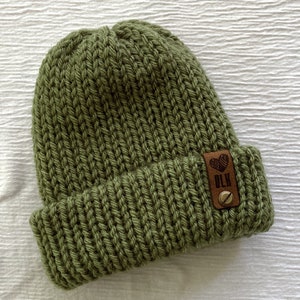 May include: A green knitted beanie with a brown leather patch that says "BLK" with a heart symbol.
