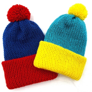 Puede incluir: Dos gorros de punto con pompones. Un gorro es azul con un borde rojo y un pompón rojo. El otro gorro es azul verdoso con un borde amarillo y un pompón amarillo.