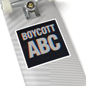 Può includere: Un adesivo bianco con la scritta "BOYCOTT ABC" in bianco, rosso e blu su sfondo nero. L'adesivo è posto su uno skateboard.