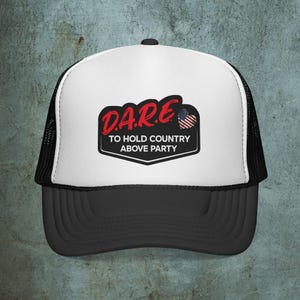 May include: A black and white trucker hat with a curved peak. The front panel is white with a black and red graphic that reads "D.A.R.E. TO HOLD COUNTRY ABOVE PARTY" with an American flag heart.