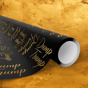 May include: A roll of black wrapping paper with the words "Dump Trump" in gold script. The paper is partially unrolled, revealing a white interior. The background is a textured gold color.