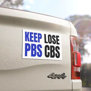 以下が含まれることがあります： 「KEEP LOSE PBS CBS」という青と黒の文字が書かれた長方形の白いバンパーステッカーが、明るい色の車の後部に貼られています。 車には赤いテールライトと4x4のエンブレムが付いています。