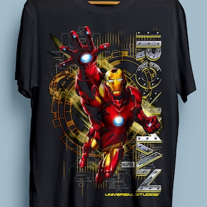 Puede incluir: Camiseta negra con un gr&aacute;fico de Iron Man volando frente a un fondo amarillo y negro. El texto "IRON MAN" est&aacute; en el lado derecho de la imagen. El texto "MARVEL" y "UNIVERSAL STUDIOS" est&aacute;n en la parte inferior de la imagen.