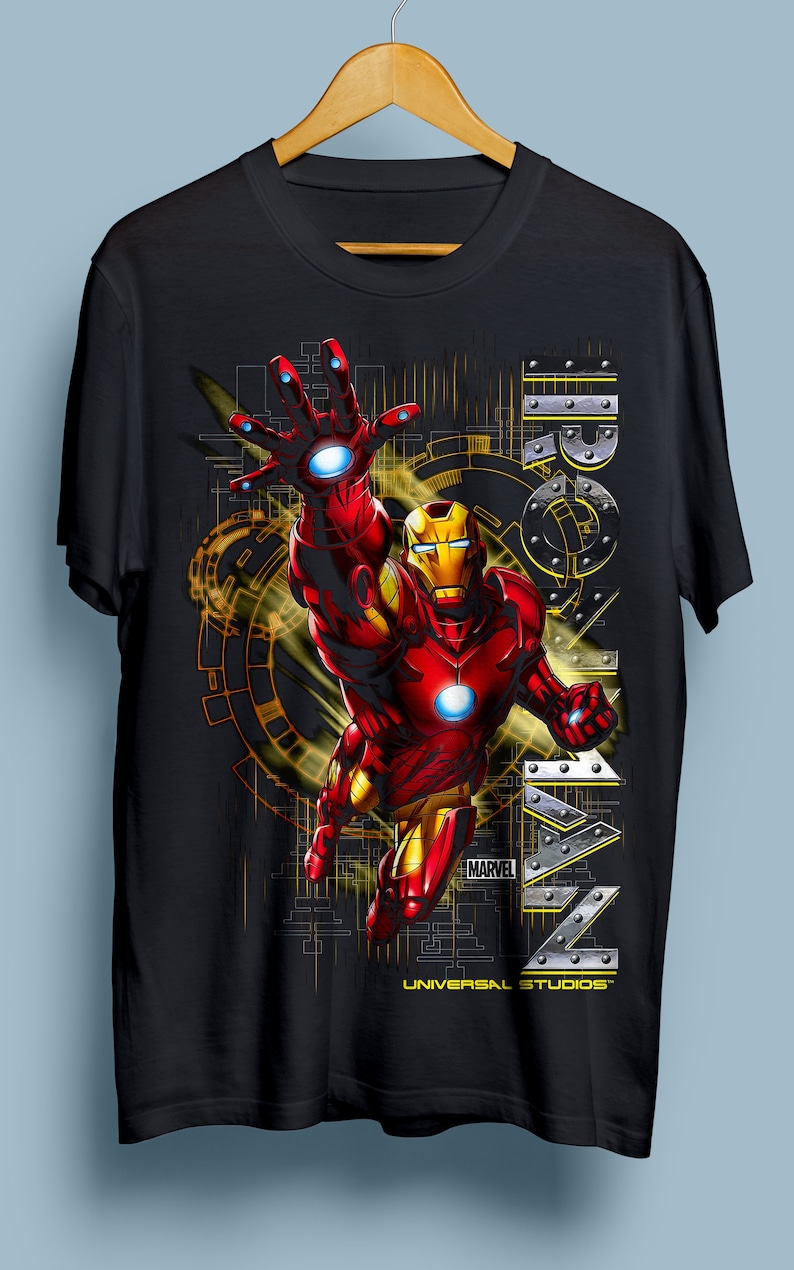 Puede incluir: Camiseta negra con un gr&aacute;fico de Iron Man volando frente a un fondo amarillo y negro. El texto "IRON MAN" est&aacute; en el lado derecho de la imagen. El texto "MARVEL" y "UNIVERSAL STUDIOS" est&aacute;n en la parte inferior de la imagen.