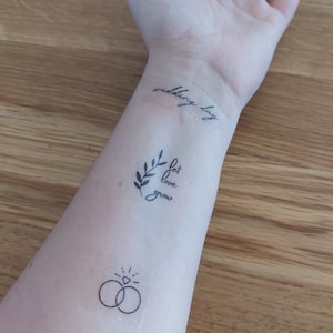 May include: A person's arm with three temporary tattoos. The tattoos are a ring with a diamond, a branch with the words "let love grow", and the words "wedding day".