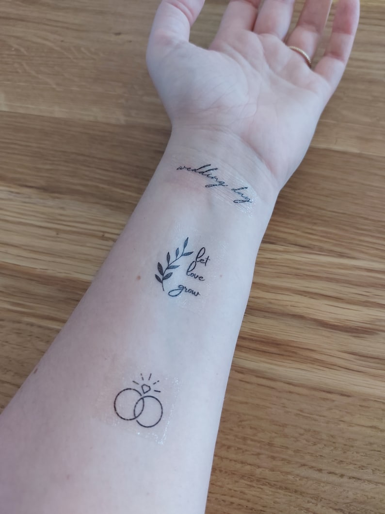 May include: A person's arm with three temporary tattoos. The tattoos are a ring with a diamond, a branch with the words "let love grow", and the words "wedding day".