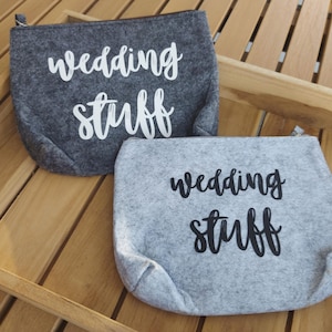 Könnte beinhalten: Zwei graue Reißverschlusstaschen aus Filz mit dem Text "wedding stuff" in weißer und schwarzer Schrift.