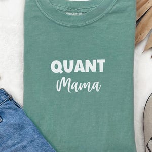 May include: A teal green t-shirt with the text "QUANT Mama" printed in white.