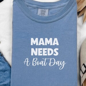 May include: A light blue t-shirt with the text "Mama Needs A Boat Day" in white.