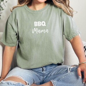 K&ouml;nnte beinhalten: Ein gr&uuml;nes T-Shirt mit dem Text "BBQ Mama" in wei&szlig;en Buchstaben.