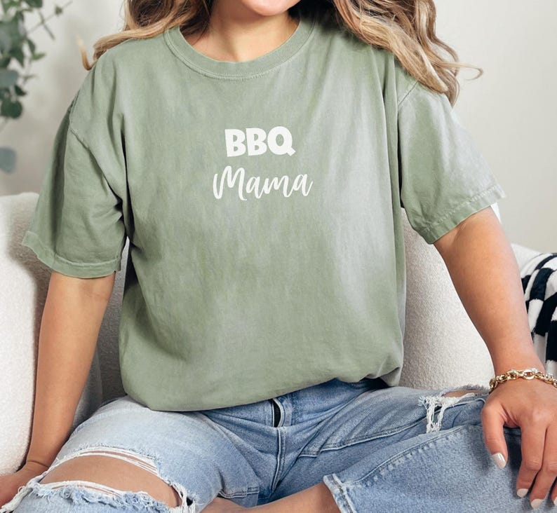 K&ouml;nnte beinhalten: Ein gr&uuml;nes T-Shirt mit dem Text "BBQ Mama" in wei&szlig;en Buchstaben.