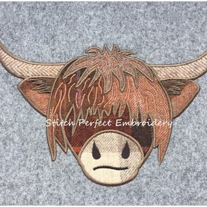 May include: Embroidered patch of a Highland cow's head with a brown and tan tartan pattern. The cow has a grumpy expression and the text "Stitch Perfect Embroidery" is below the cow.