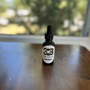 May include: A black glass bottle with a dropper top and a white label. The label has a black and white illustration of a man with a beard and the text "38 Beard Products Volume 2".