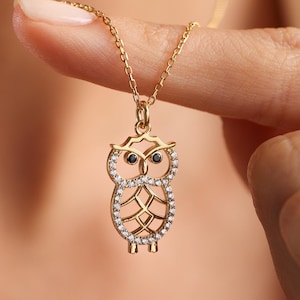 Op de afbeelding: Een gouden ketting met een delicate uil hanger versierd met heldere en zwarte zirkonia stenen.