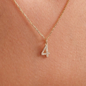 May include: A gold chain necklace with a small pendant shaped like the number four. The pendant is covered in tiny clear stones.