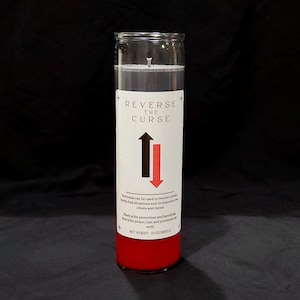 May include: A tall cylindrical glass candle with red wax, featuring a white label that reads REVERSE THE CURSE with a black upward arrow and a red downward arrow. The label includes descriptive text and a net weight of 13 ounces.