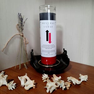 May include: A red and black candle with the words "Reverse the Curse" and an arrow pointing upwards and downwards. The candle is on a black candle holder.