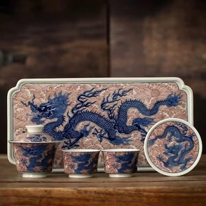 Può includere: Servizio da tè in porcellana blu e bianca con motivo a drago. Il set comprende un vassoio, una teiera con coperchio, due tazze da tè e un sottobicchiere. Il vassoio ha uno sfondo a onde rosa e bianche.