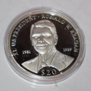 May include: A silver commemorative coin featuring a portrait of Ronald Reagan, the 40th US President. The coin has the text "40th US President Ronald W. Reagan 1981-1989" and "$20" inscribed on it.