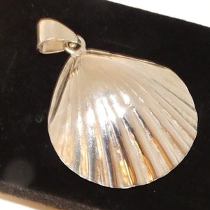 May include: A silver pendant in the shape of a seashell, with detailed ridged texture. The pendant has a loop at the top for a chain. The seashell design is a classic nautical theme, suitable for jewelry.