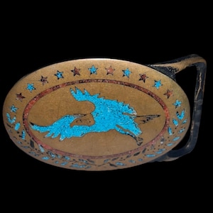 May include: Oval-shaped belt buckle with a bronze finish and a turquoise inlay depicting a running animal. The buckle is decorated with red and blue stars and floral patterns. The buckle's dimensions are approximately 3 inches by 2 inches.