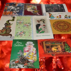May include: A collection of vintage greeting cards featuring various holiday and seasonal illustrations, including a fireplace, a candy jar with a pinecone, floral patterns, a person holding a rose, and a circular gold design with an eagle motif.
