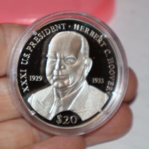 May include: A silver commemorative coin featuring a portrait of Herbert Hoover, the 31st U.S. President. The coin has the text "XXXI US PRESIDENT HERBERT C. HOOVER 1929 1933" around the portrait and "$20" at the bottom.