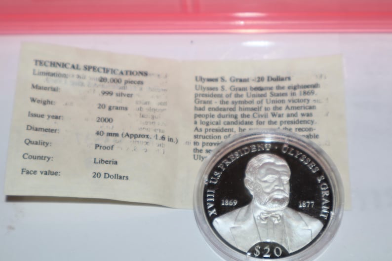 May include: A silver proof coin commemorating Ulysses S. Grant, the 18th president of the United States. The coin features a portrait of Grant and the text "XVIII US. PRESIDENT OLYSSES S. GRANT 1869 1877" around the edge. The coin is 40 mm in diameter and has a face value of 20 dollars.