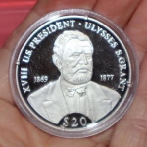 May include: A silver commemorative coin featuring a portrait of Ulysses S. Grant, the 18th US President. The coin has the text "XVIII US PRESIDENT ULYSSES S. GRANT" and the years "1869" and "1877" inscribed around the portrait. The coin also has the text "$20" at the bottom.