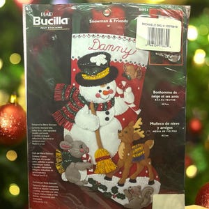 May include: A Plaid Bucilla felt stocking kit featuring a snowman and friends design. The kit includes stamped felt, cotton floss, sequins, and beads. The stocking is 18 inches long and includes the name "Danny".