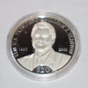 May include: A silver commemorative coin featuring a portrait of William J. Clinton, the 42nd U.S. President. The coin has the text "XII US PRESIDENT WILLIAM J. CLINTON 1993 2001" around the edge and "$20" in the center.