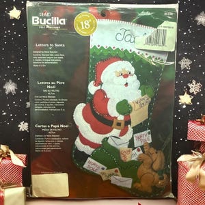 May include: A Bucilla felt stocking kit, 18 inches, featuring a Santa Claus design. The kit includes stamped felt, cotton floss, sequins, and beads. The stocking has a green background with letters to Santa and a dog.