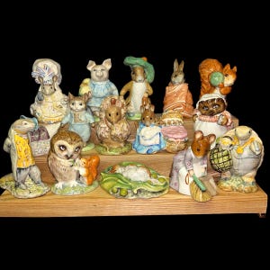 May include: A collection of ceramic figurines featuring various animal characters. The figurines are arranged on a wooden shelf and include a pig, rabbit, squirrel, owl, and other creatures. The figurines are painted with bright colors and detailed features.